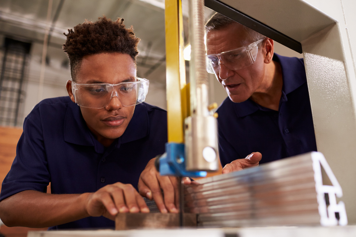 Carpenter Training Male Apprentice To Use Mechanized Saw